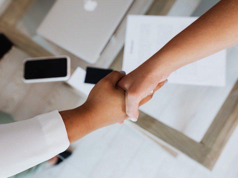 Handshake over a desk with technology and documents