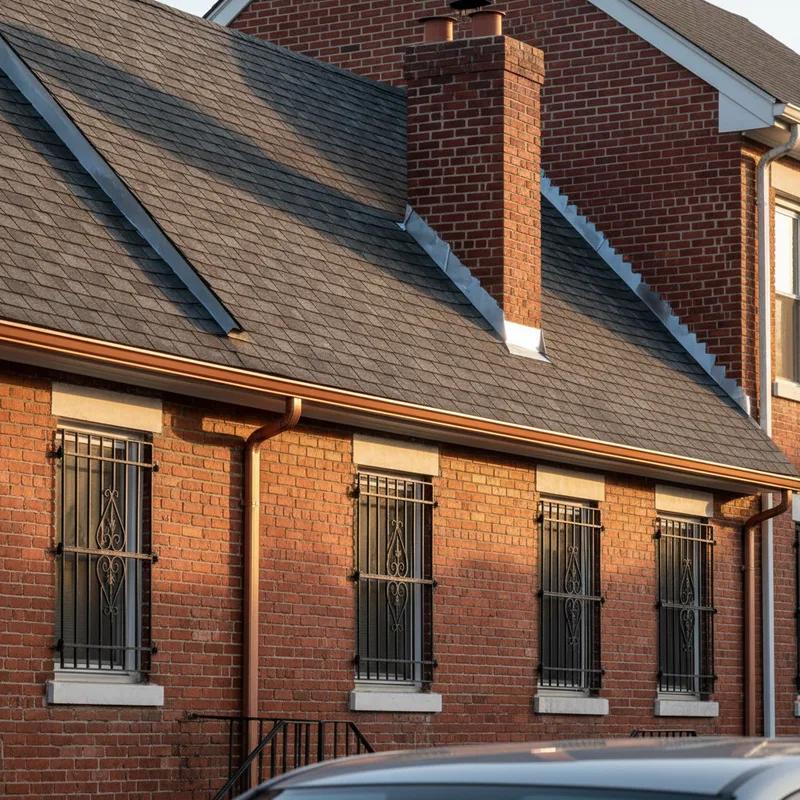 A roofing crew completing a new shingle roof installation on a Philadelphia row home while a city building inspector reviews the permitted work on a tablet